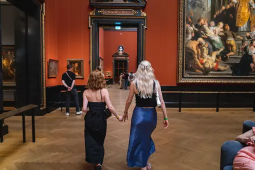 Two young women walk hand-in-hand through the Picture Gallery of the Kunsthistorisches Museum. 