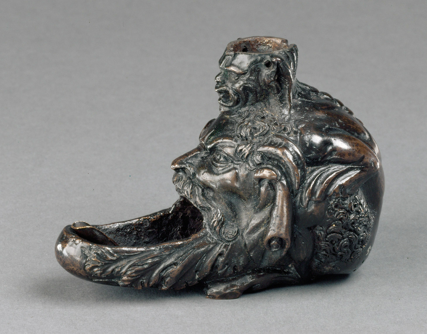 Öllampe in Gestalt eines hockenden Satyrs mit groteskem Maskeron zwischen den Knien