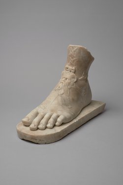 Linker Fuß mit Sandale auf Plinthe