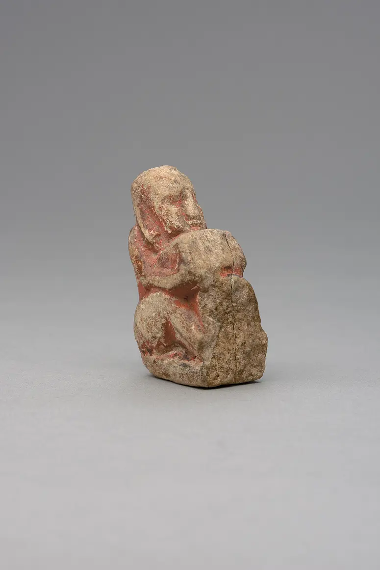 Hockender, nackter Mann, über seinem Phallus eine Stele haltend, fragmentiert