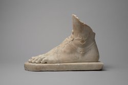 Linker Fuß mit Sandale auf Plinthe