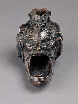 Öllampe in Gestalt eines hockenden Satyrs mit groteskem Maskeron zwischen den Knien
