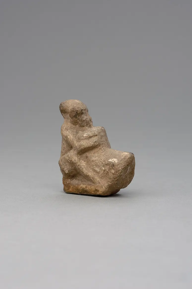 Hockender, nackter Mann, über seinem Phallus eine Stele haltend, fragmentiert