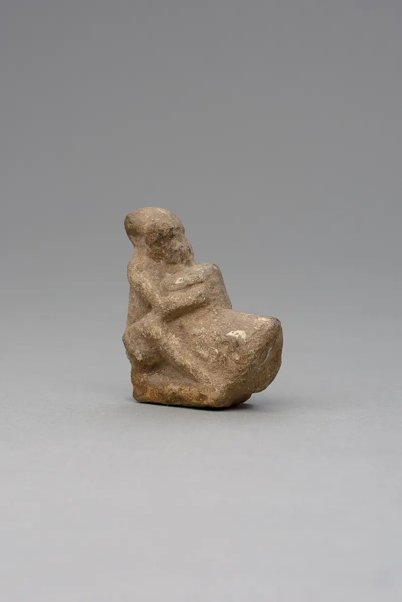 Hockender, nackter Mann, über seinem Phallus eine Stele haltend, fragmentiert