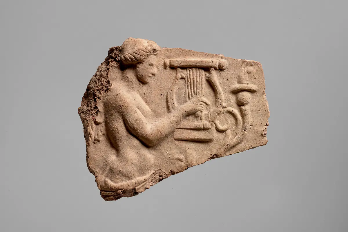 Fragment einer Aufsatzplatte(?) mit Darstellung von musizierenden Flügelfrauen in Ranken. Flügelfrau mit Kithara